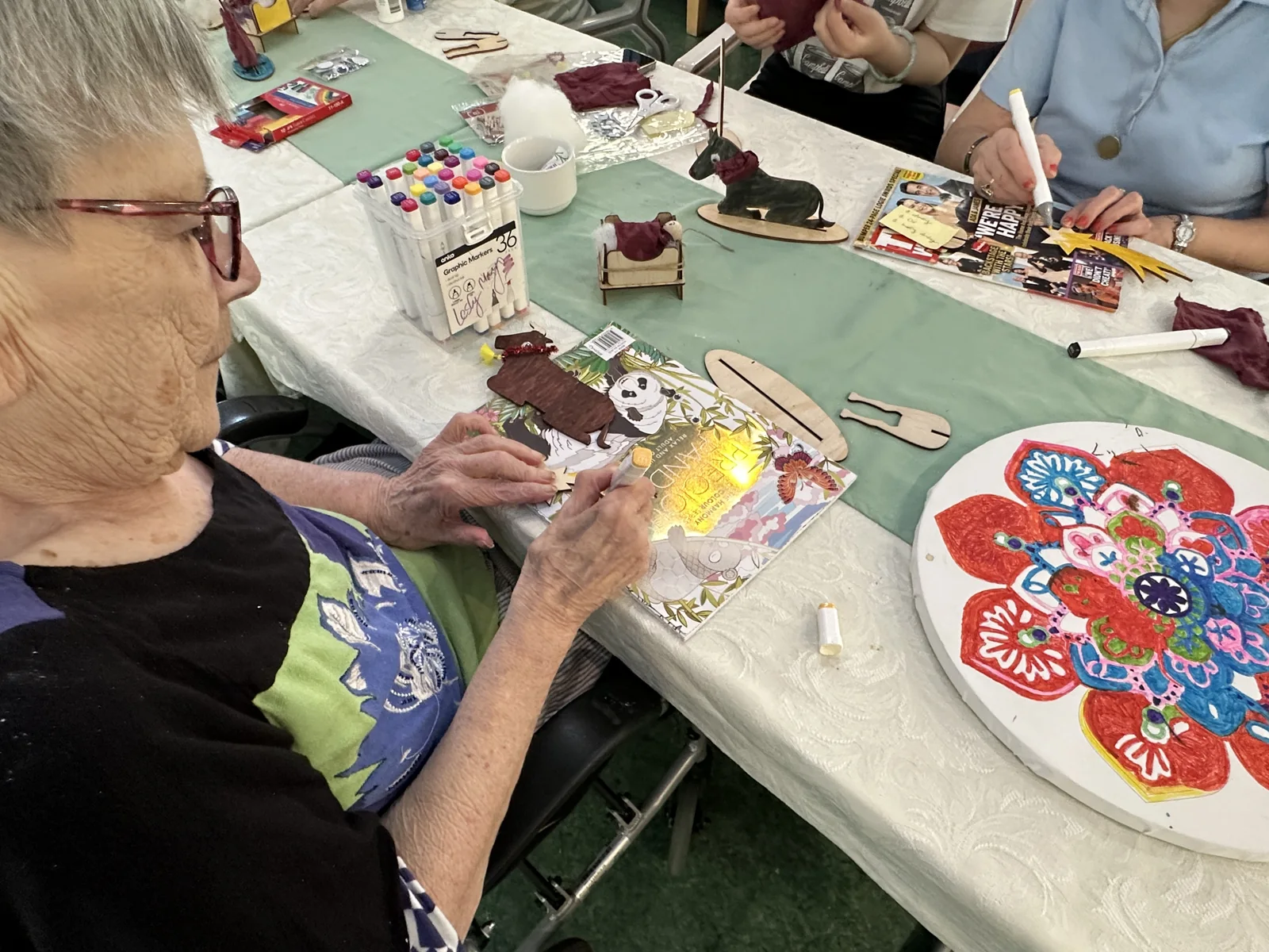 A resident adding colour to a wooden Nativity figure at a table of craft materials