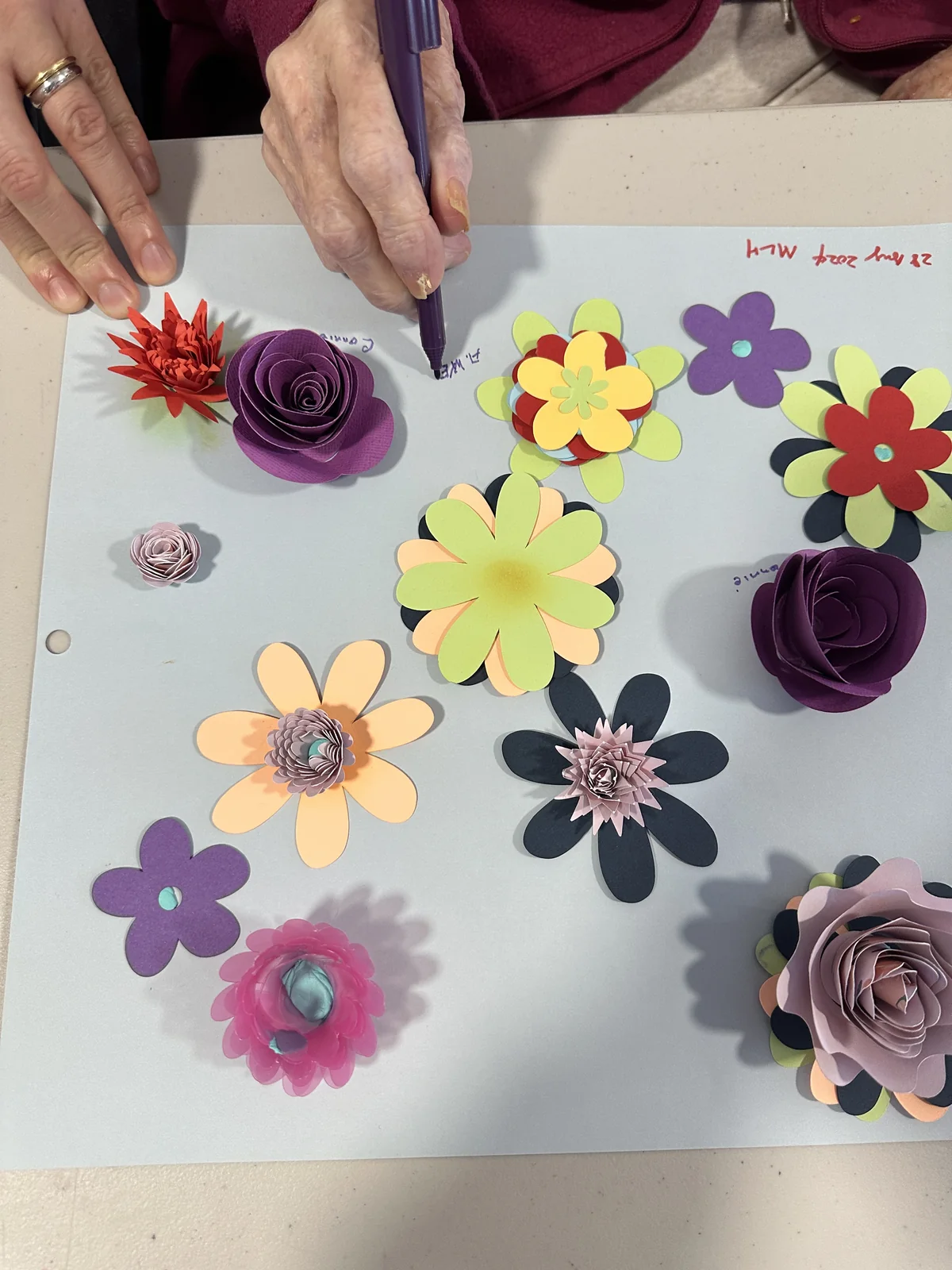 Hands arranging colourful paper flowers on a shared board