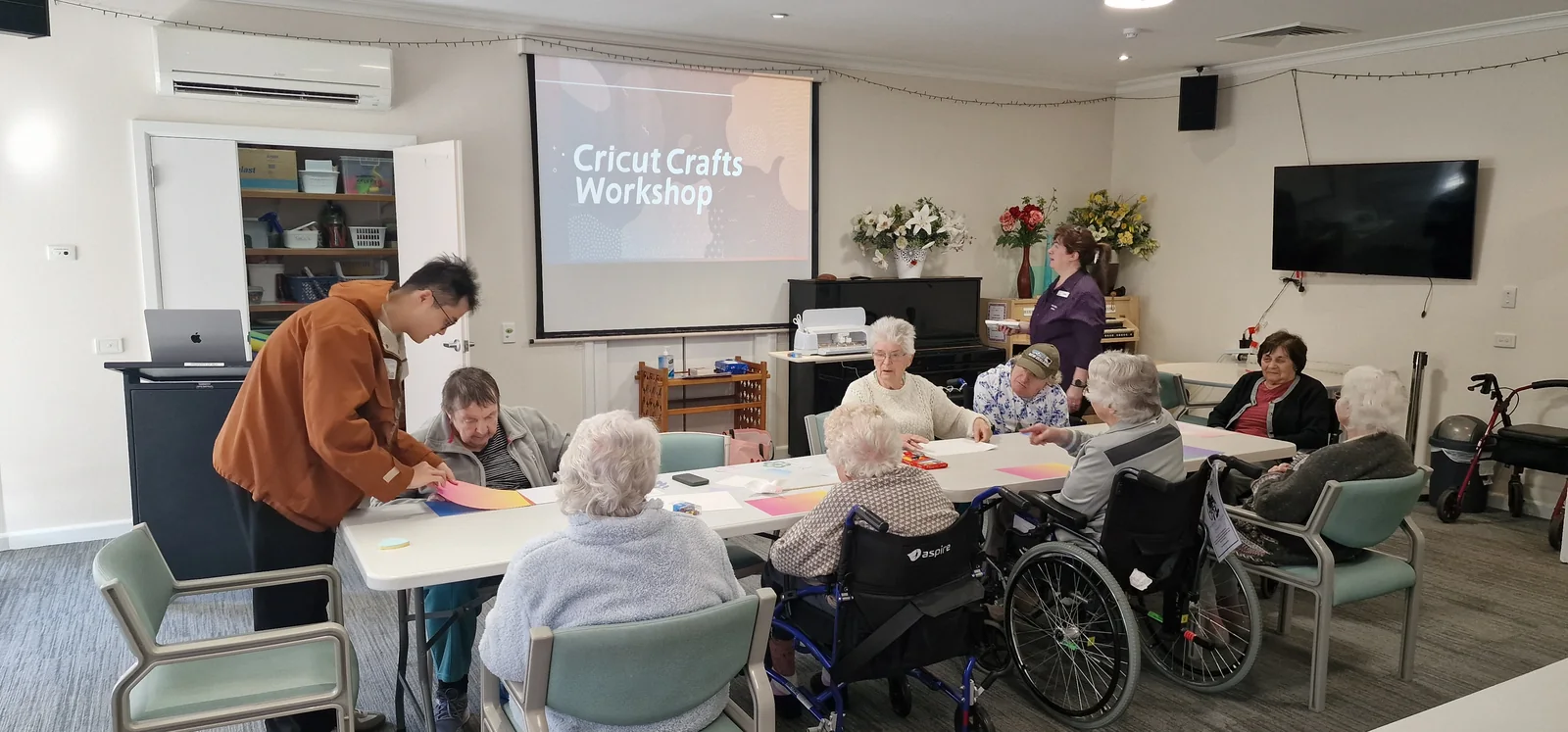 A shared Cricut crafting workshop with residents seated around a table of paper materials