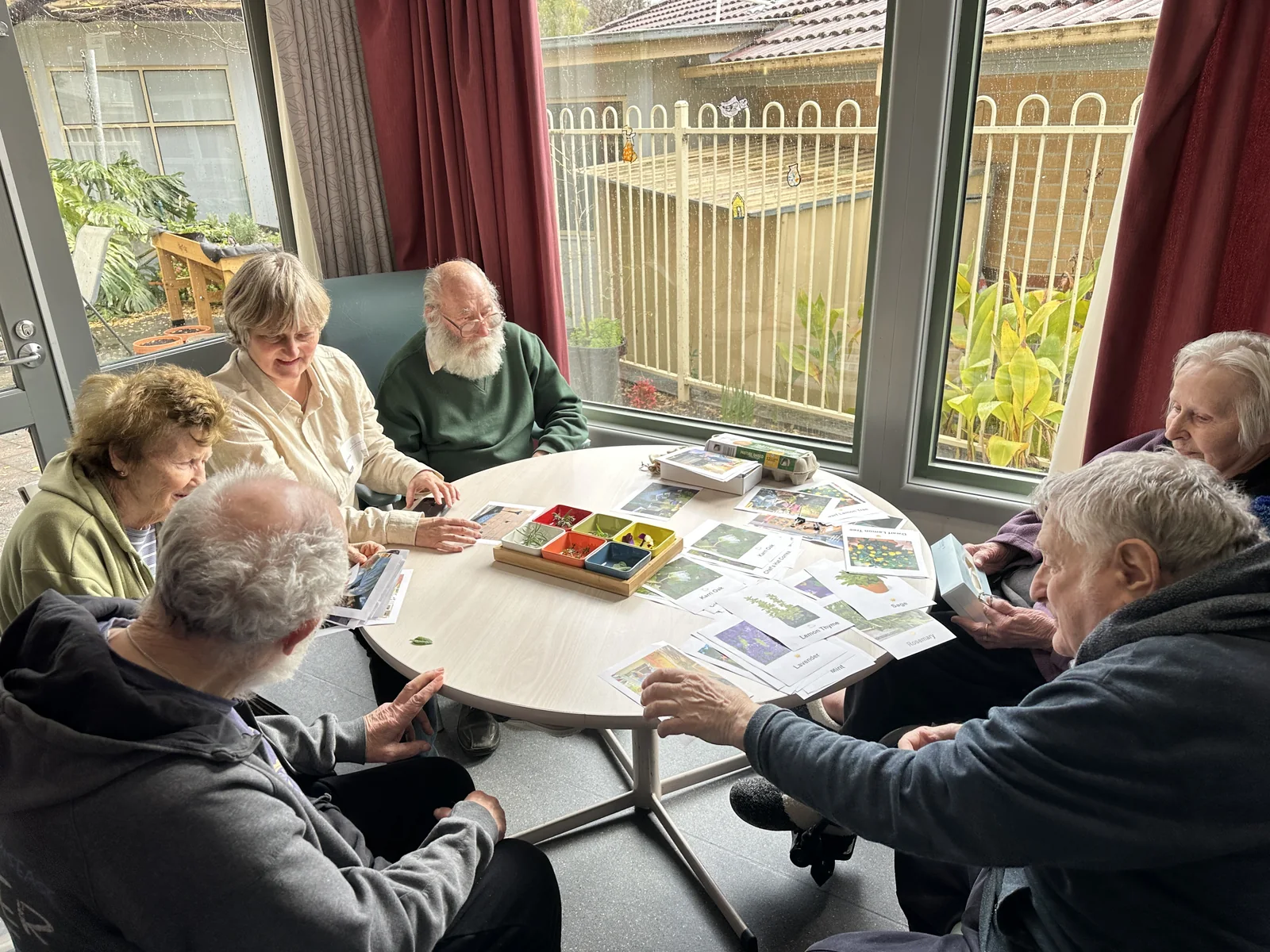 Residents and a facilitator around an indoor table with photographs and small trays of materials
